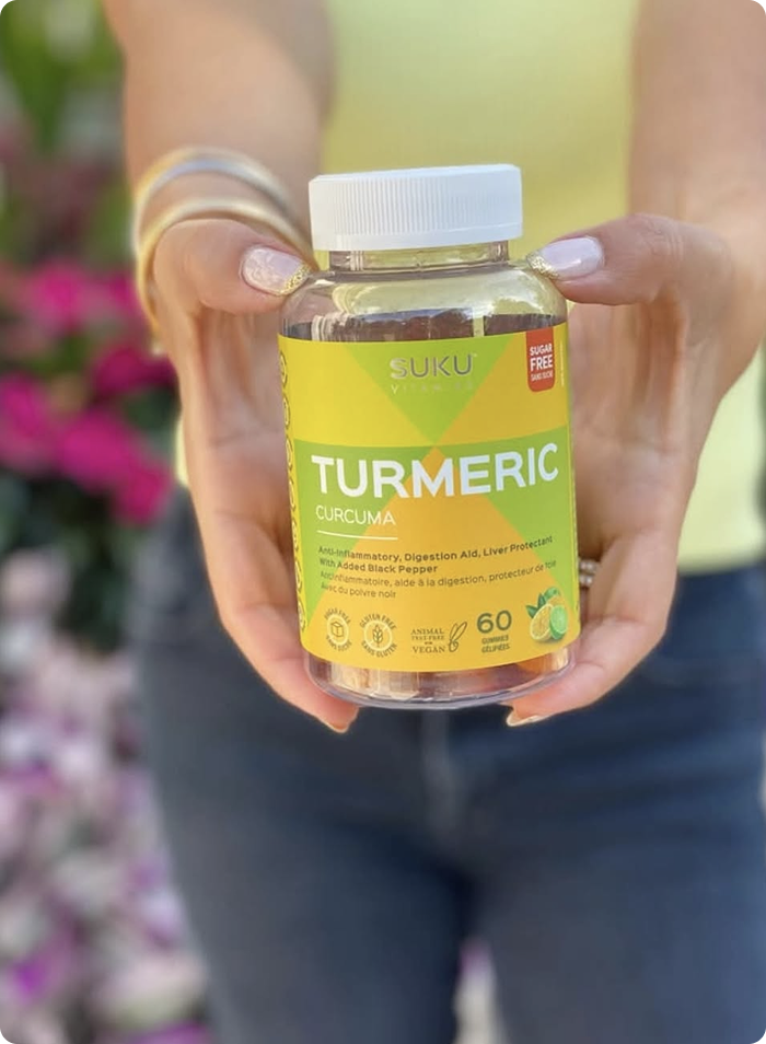 Person holding a bottle of SUKU Turmeric Curcuma supplements with a blurred floral background