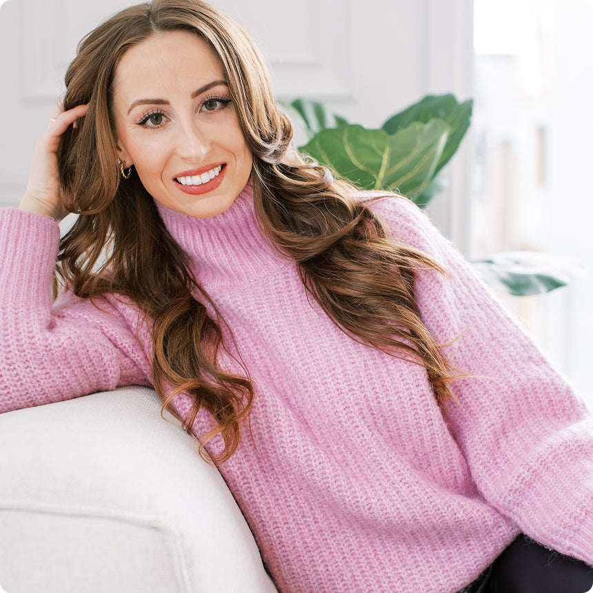 marlee wearing a pink sweater sitting on a couch with a blurred indoor background