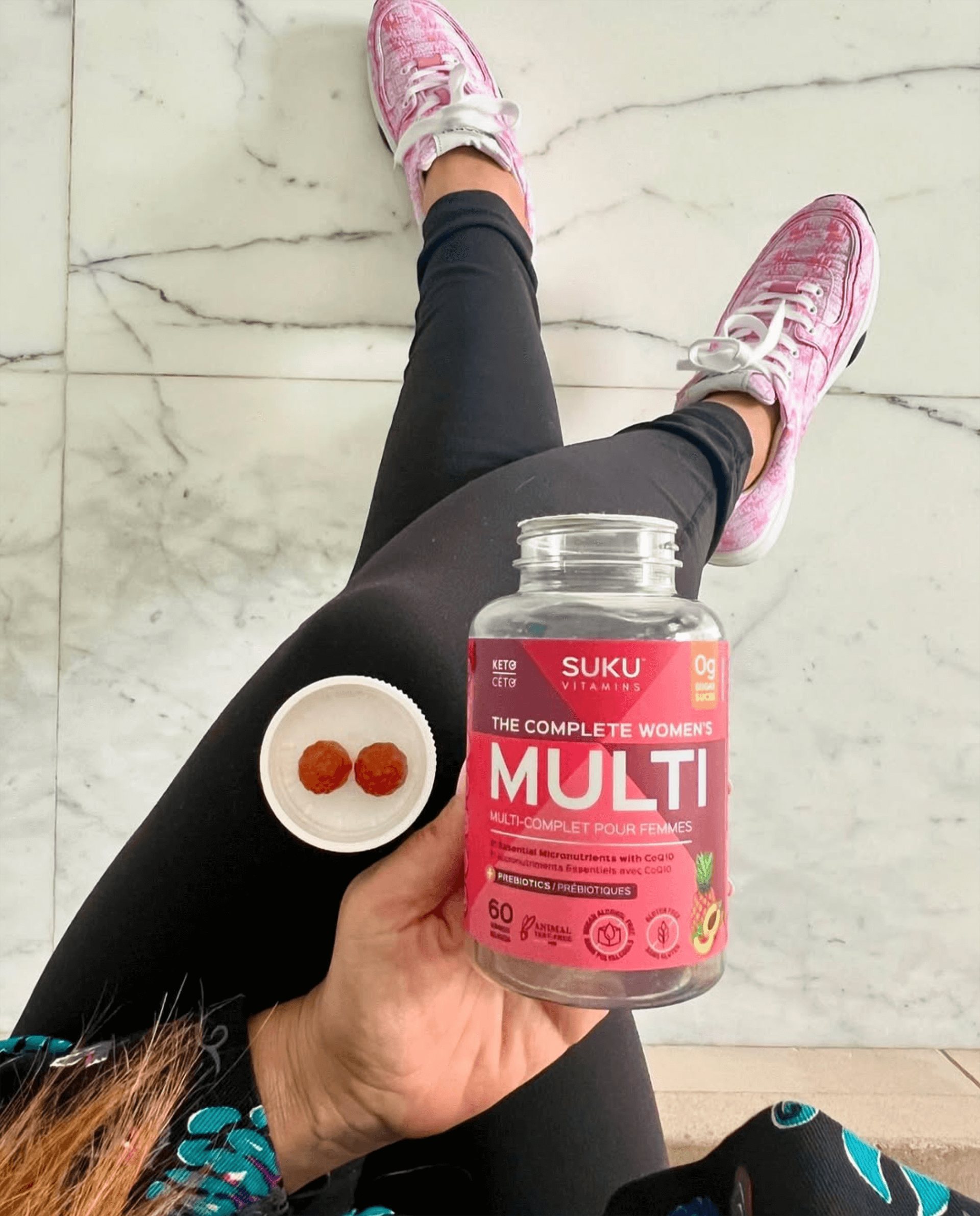 Person holding a Suku Vitamins Multi supplement bottle on a marble floor.